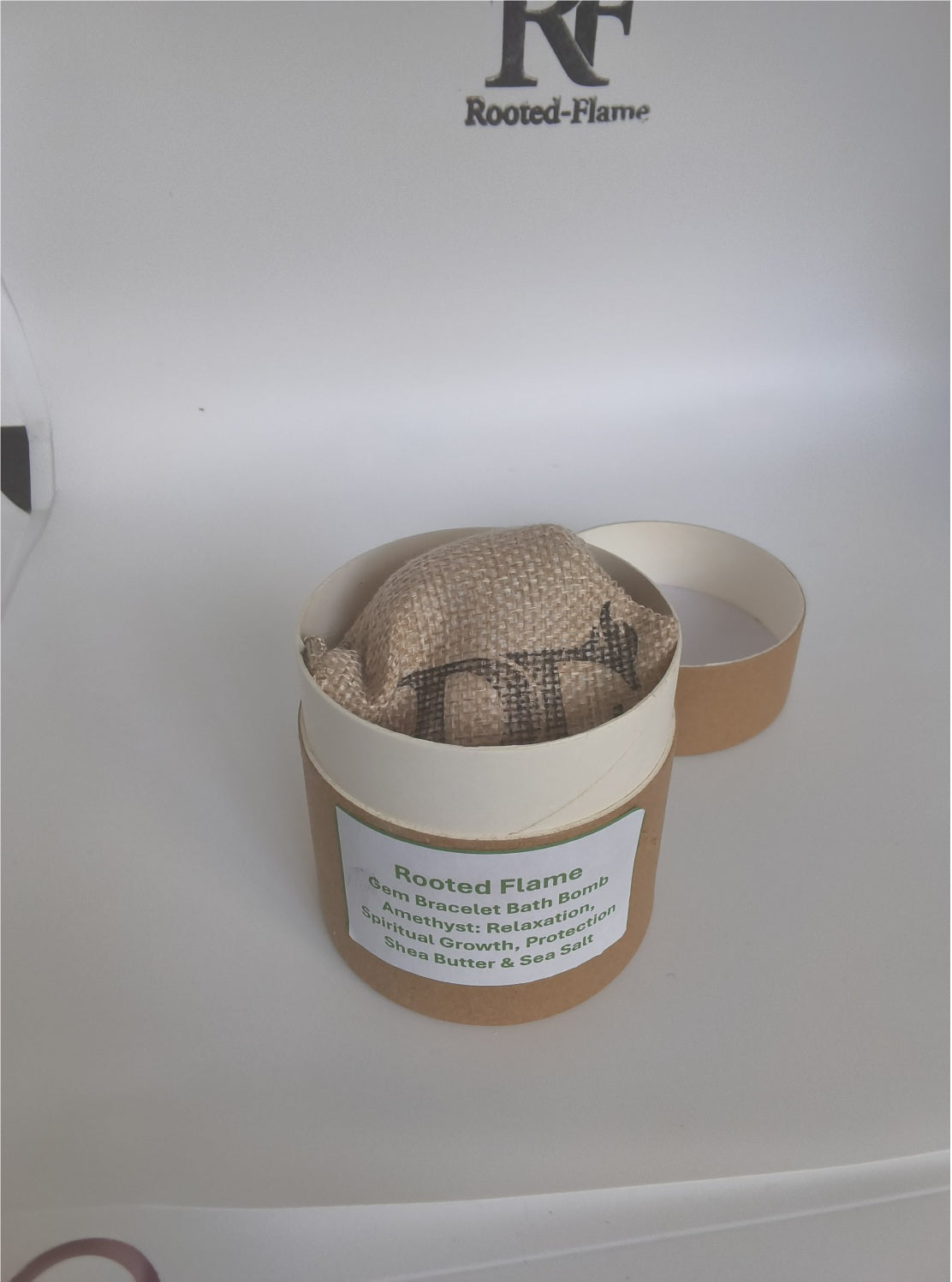 Rooted Flame Amethyst Gemstone Bracelet Bath Bomb in burlap bag beside branded packaging